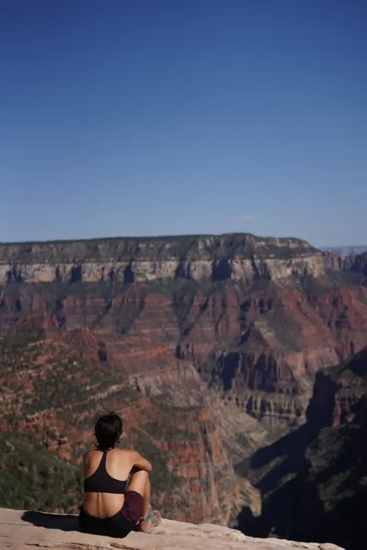 Someone sitting on the rim of the Grand Canyon, red cliffs below