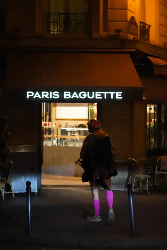 A lit Paris Baguette shopfront at night with someone walking past