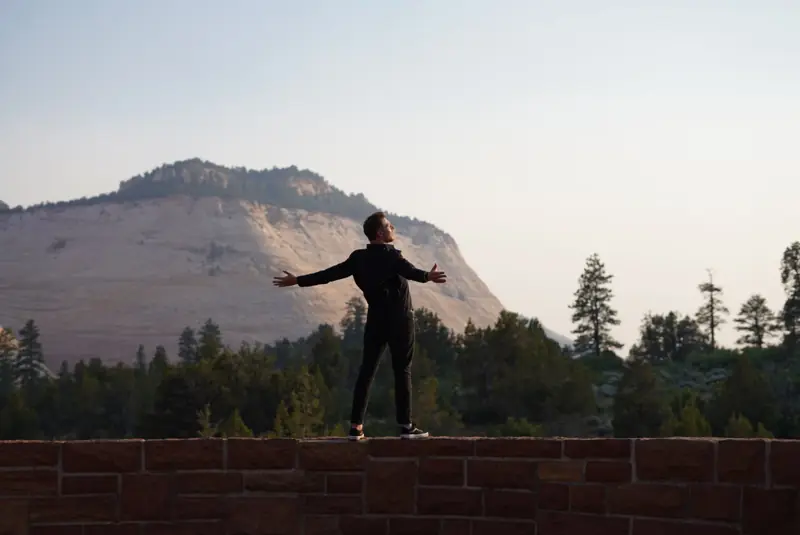 Pavel with his arms wide open on a wall in front of a mountain in Zion